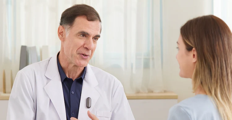 A physician wearing a Plaud NotePin S on his coat while talking with a patient.